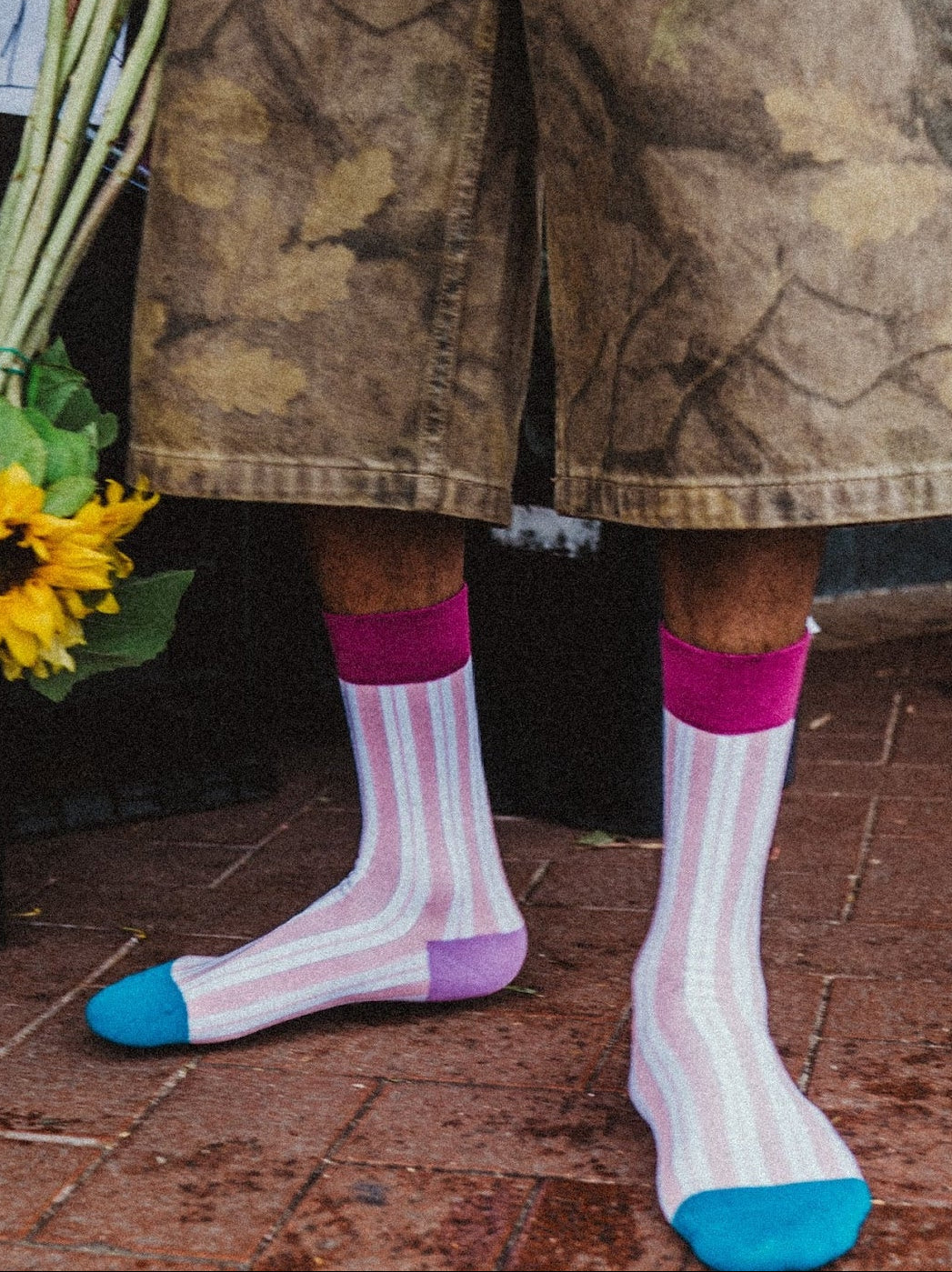 Person wearing camouflage shorts and colorful socks, holding sunflowers.